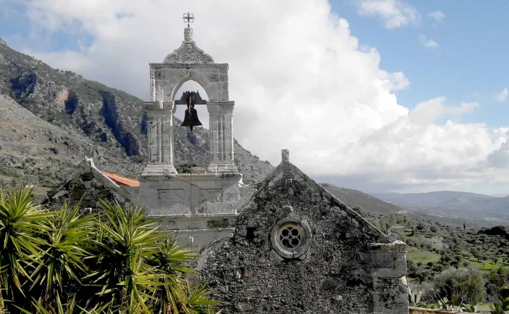 Monastery of Vrontisi: The belltower of Vrontisi Monastery under the blue sky with few clouds and the mountains as the background.